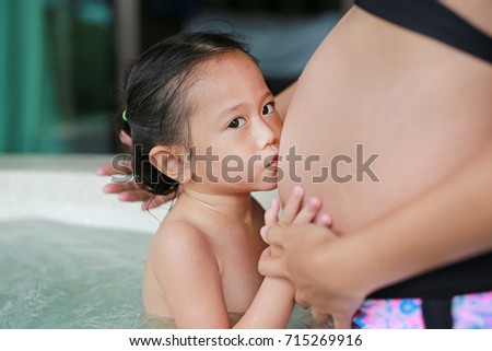 Child girl kissing belly of pregnant women in hot tub.