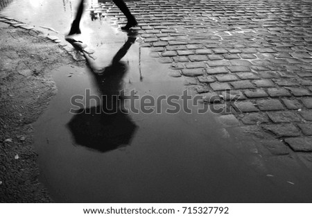 Reflection of woman with umbrella in the puddle during rainy day