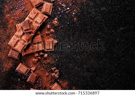 Broken chocolate pieces and cocoa powder on marble. The chunks of chocolate over dark background Royalty-Free Stock Photo #715336897
