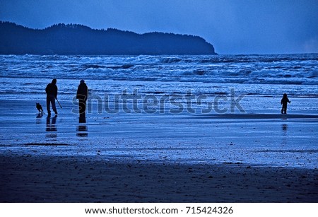 deep blue twilight on oregon coast with silhouettes of a family of two adults a child and a dog standing on wet sandy beach as the tide goes out