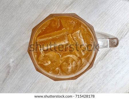 Cold glass of iced tea with ice cubes, isolated on wooden background.