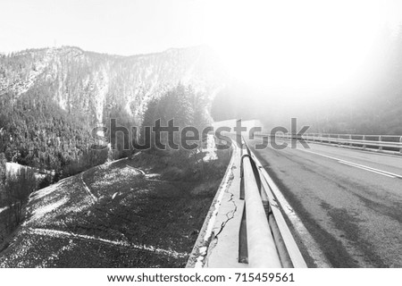 Highway in Piedmont on the background of snow capped Italian Alps. View of the mountain valley with asphalt road at sunrise. Black and white picture 