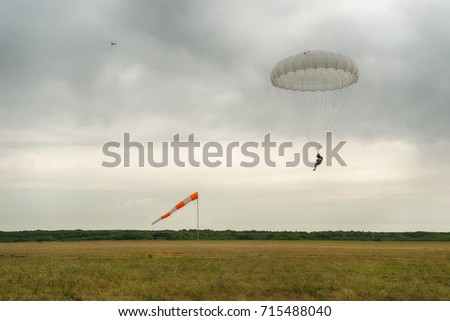 Military parachute jumper on cloudy sky landing background.