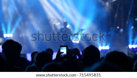 fans take photos and record videos with modern smartphones during the live concert of a rock band