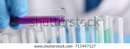 A male chemist holds test tube of glass in his hand overflows a liquid solution of potassium permanganate conducts an analysis reaction takes various versions of reagents using chemical manufacturing Royalty-Free Stock Photo #715497127