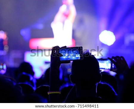 fans who take photos and record videos with modern smartphones during the live concert of a rock band