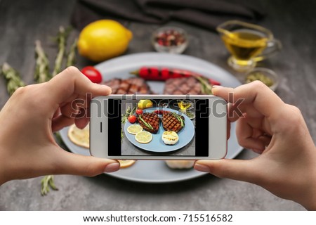 Woman taking photo of yummy grilled steaks at kitchen table