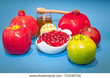 Jewish symbols, the Jewish New Year Rosh Hashanah concept - apple shaped plate with red pomegranate seeds on a blue background with honey. Rosh Hashanah greeting.