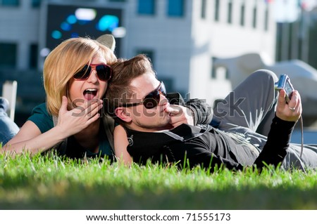 Young emotional happy teenage couple taking picture on grass in city park