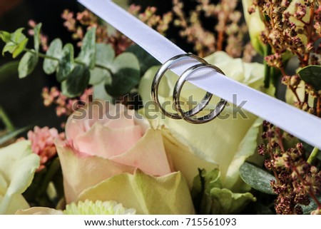 A detail picture of the wedding rings on the bride´s flower bouquet  full of roses and other nice flowers. 