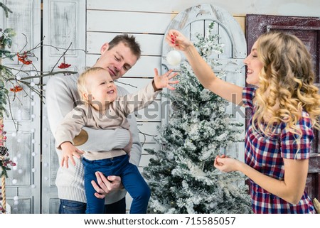 Portrait of happy family: mom, dad and little son. Dad holding laughing son on hands and mom showing to him a Christmas toy. Concept of Merry Christmas and New Year