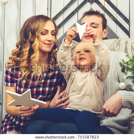 Portrait of young family: mom, dad and little son. All of them sitting in decorated room, boy holding and playing with wooden star, toned image. Concept of Merry Christmas and New Year
