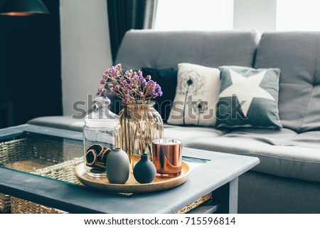 Home interior decor in gray and brown colors: glass jar with dried flowers, vase and candle on the wooden tray on the coffee table over sofa with cushions. Living room decoration. Royalty-Free Stock Photo #715596814