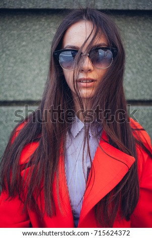 girl in a shirt of white pants and a red coat on the street in glasses, smiles positive