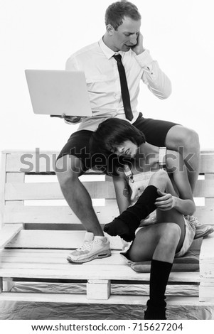 young couple of handsome busy man speaks on cell phone or businessman and pretty woman or girl working on portable laptop in shirt and tie, sits on wooden bench at home isolated on white background