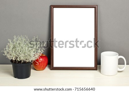 Brown frame mockup with plant pot, mug and apple on wooden shelf. Empty frame mock up for presentation design. Template framing for modern art.
