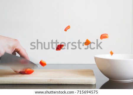 Person or cook cutting vegetables. Pieces of bell pepper or paprika shoot into a bowl. All white background.