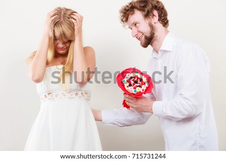 Handsome man giving pretty sad depressed woman candy bunch bouquet flowers. Unhappy couple.