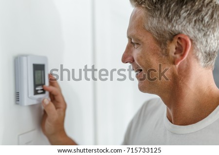 Smiling Man Adjusting Thermostat On Home Heating System Royalty-Free Stock Photo #715733125