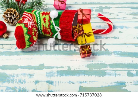 Christmas stocking and branch of spruce with cones lies on a white-blue wooden surface. From it stick out gifts and a stick. Top view. Horizontal shot.