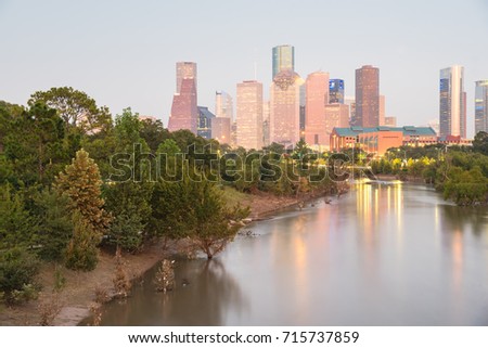 Fast water in Bayou River with downtown Houston, Texas, USA skylines city lights reflection at sunset/twilight. Debris, tree down branches from Hurricane Harvey are spot/available on both river banks
