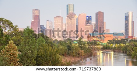 Fast water in Bayou River with downtown Houston skylines city lights reflection at sunset/twilight. Debris, tree down branches from Hurricane Harvey are spot/available on both river banks. Panorama