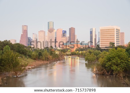 Fast water in Bayou River with downtown Houston, Texas, USA skylines city lights reflection at sunset/twilight. Debris, tree down branches from Hurricane Harvey are spot/available on both river banks
