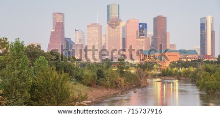 Fast water in Bayou River with downtown Houston skylines city lights reflection at sunset/twilight. Debris, tree down branches from Hurricane Harvey are spot/available on both river banks. Panorama