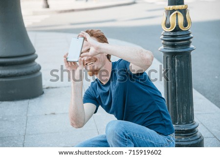 young man making photo and video on phone on the city street in summer day