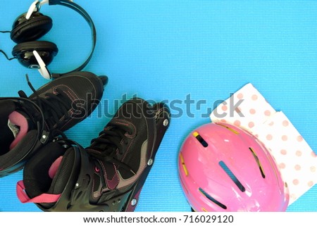 Roller skates of pink tone,Rollerblade set with pink helmet, black head phone on blue background,top view with copy space
