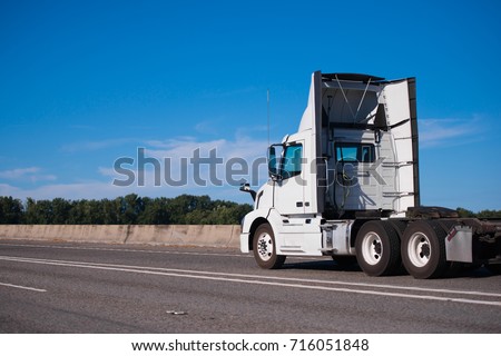 Standard big rig semi truck for local transportation of goods and commercial cargos with aerodynamic spoilers along perimeter of the day cabin to reduce air resistance and save fuel running on highway Royalty-Free Stock Photo #716051848