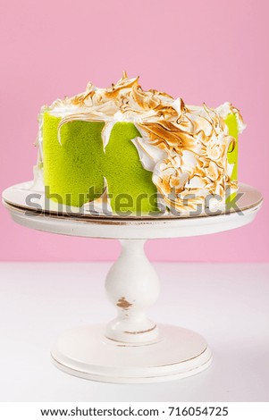 Green cake decorated with burned meringue on cake stand on pink background. Birthday cake with Italian meringue