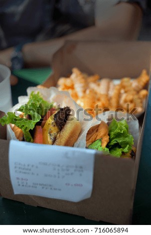 Two fast food hamburgers and french fries in a cardboard box with background arm