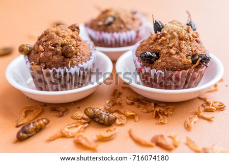 Banana cupcakes with worm insect and crispy shallots fried on orange tablecloth background. Healthy meal high protein diet concept. Selective focus.