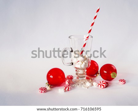 Christmas greeting card with decoration on white background. Red balls ornaments and candy. Cup with marshmallow and striped paper straw