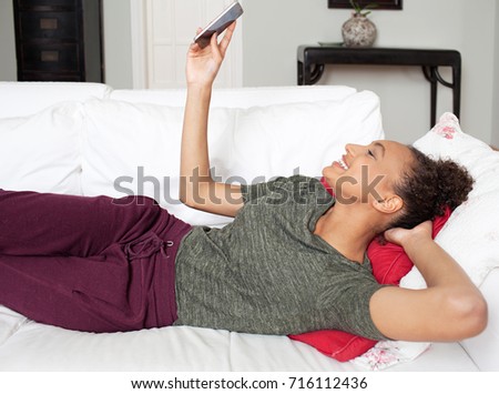 Beautiful african american teenager young woman holding smart phone taking selfies photos, joyful expression, networking in home interior. Young black female using technology, recreation lifestyle.
