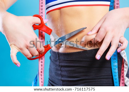 Weight gain diet liposuction concept. Woman with measure tapes pinches in the fat at the waist, holding scissors cut fold skin