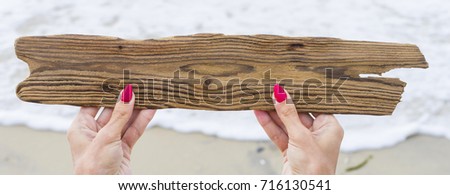 Grungy antique wooden plank in woman's hands on beach. Place empty for text. Sales and advertising concept. Travel background image.