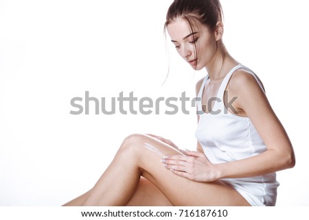 Young brunette woman in a white shirt and panties applies cream on your legs, isolated on white background