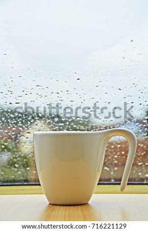 cup standing in front of a window with water drops on it
