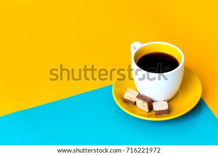 Pastel office desk with biscuit and a cup of black coffee on two tone background