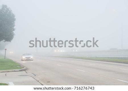 Morning foggy city frontage road with traffic sign and car silhouette in Humble, Texas, USA. Driving with caution in bad weather. Hazy transportation hazard. Severe weather theme concept background