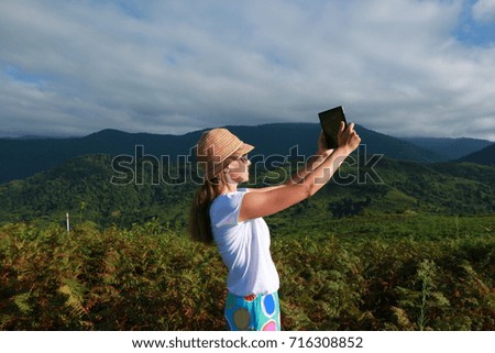  young woman in a hat from the sun takes a photograph with a tablet in the mountains