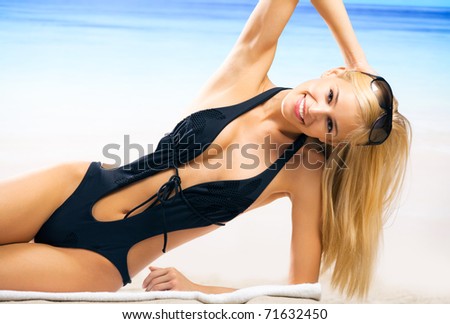 Portrait of young beautiful tanned woman in sunglasses and bikini laying during sunbath on sea beach