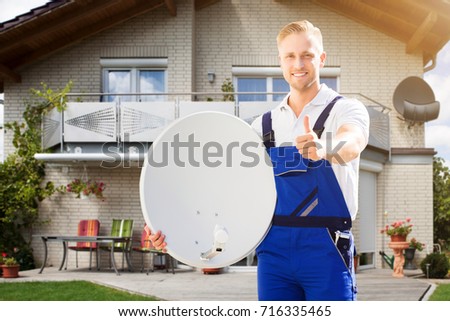 Smiling Young Man Standing Outside The House Holding Satellite Dish Showing Thumb Up Sign