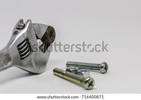 Image of isolated silver adjustable wrench gripping rusty greasy nut. Chrome bolts and nuts on white surface. Selective focus on rusty nut. Others in blur. White background.