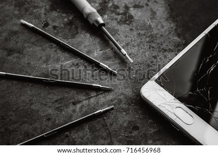 Smartphone with a broken screen and repair tools on the dark background. Close-up.