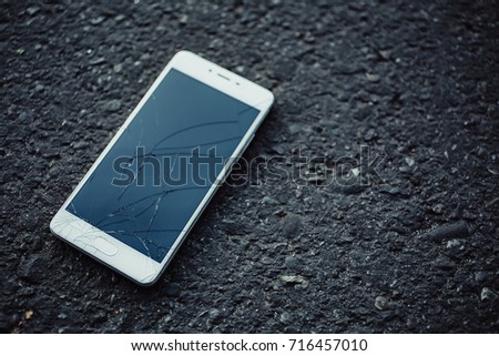 Smart phone with broken screen on dark background.