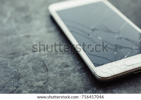 Smart phone with broken screen on dark background. Close-up.
