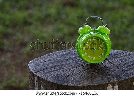 Green table clock on wooden stump with nature background, selective focus 